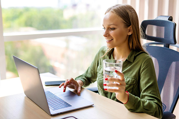 Person Holding a Glass of Water Looking at Laptop Admiring Water Utility Digital Transformation By Chateaux